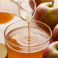 Amber apple cider vinegar pouring beside red and green apple pieces in a square frame